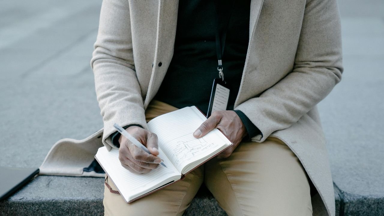 A person writing on a notebook on his lap