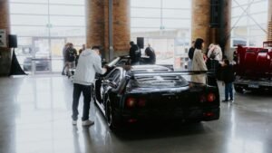 a cinfused person lookin at the cars in a car show room while other customers are busy examining a car.