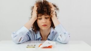 Young woman holding her head in stress while reviewing bills and counting money