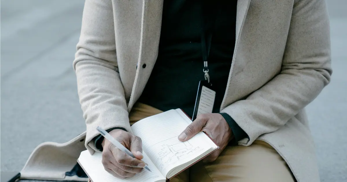 A person writing on a notebook on his lap