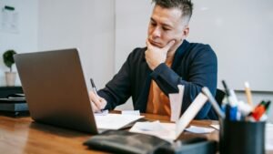 A person sitting at table with a laptop and thinking