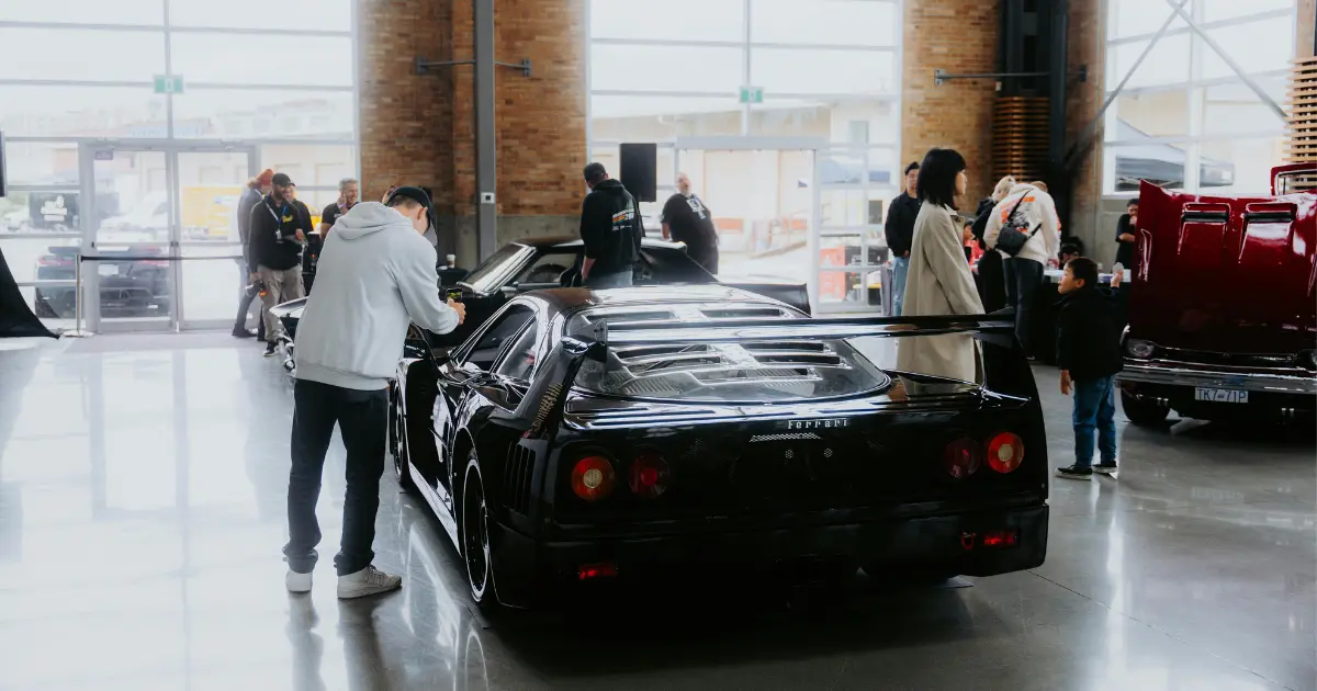 A confused person looking at the cars in a car show room while other customers are busy examining a car.